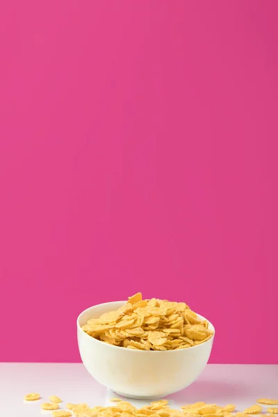 Vista de cerca de un tazón blanco lleno de sabrosos copos de maíz dulces en rosa - foto de stock