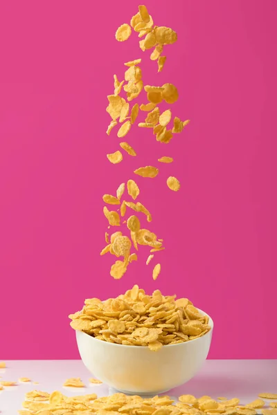 Close-up view of tasty corn flakes falling into white bowl on pink — Stock Photo