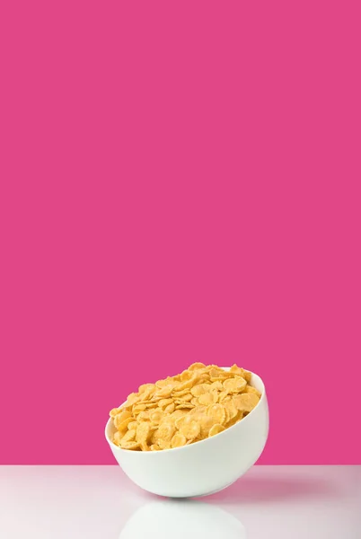 Vista de cerca de un tazón blanco lleno de sabrosos copos de maíz saludables en rosa - foto de stock