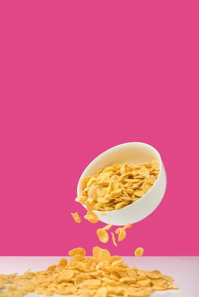 Nahaufnahme einer weißen Schüssel mit Cornflakes, die sich auf rosa ausschütten — Stockfoto