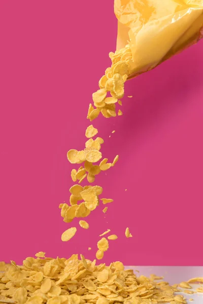 Close-up view of corn flakes pouring out from bag on pink — Stock Photo