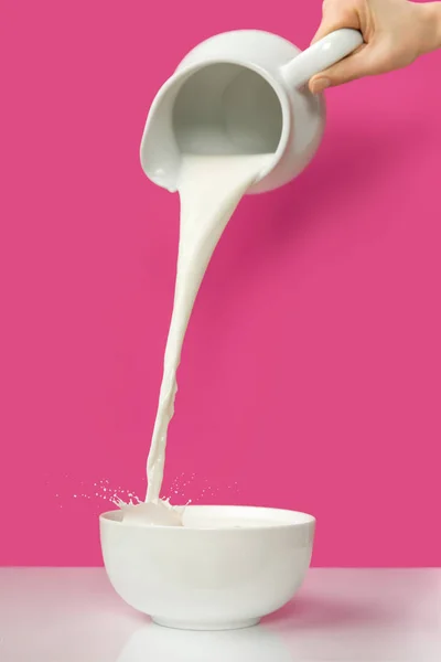 Cropped shot of hand pouring fresh natural milk from jug to bowl on pink — Stock Photo