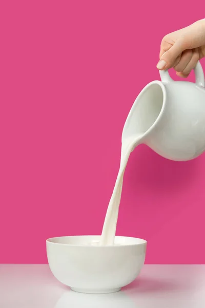 Partial view of hand pouring fresh organic milk from jug to bowl on pink — Stock Photo