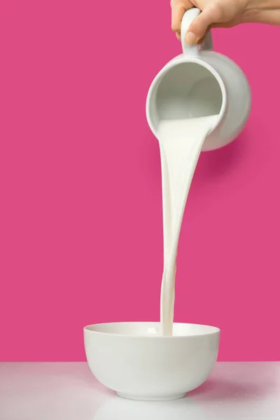 Abgeschnittene Hand gießt frische Bio-Milch aus Krug in Schüssel auf rosa — Stockfoto
