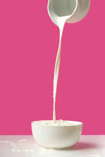 Pouring fresh healthy milk from jug to bowl on pink — Stock Photo