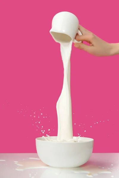 Partial view of person pouring fresh healthy milk from jug to bowl on pink — Stock Photo