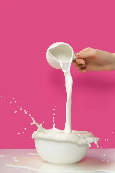 Tiro cortado de pessoa derramando leite saudável fresco de jarro para tigela em rosa — Fotografia de Stock