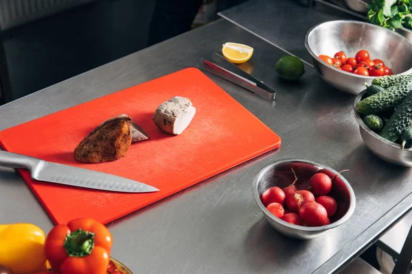 Carne en rodajas en la tabla de cortar con verduras en la cocina del restaurante - foto de stock