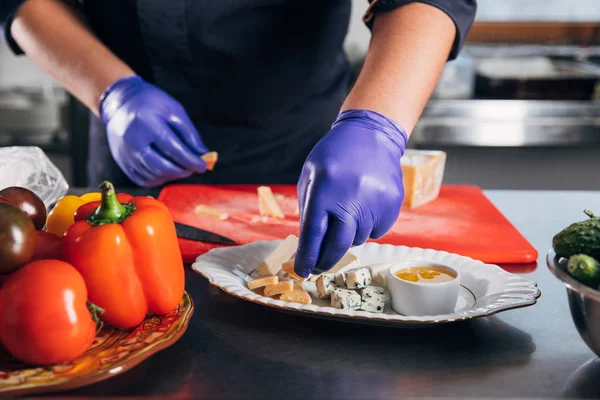 Recortado tiro de chef poner rebanadas de queso en el plato - foto de stock