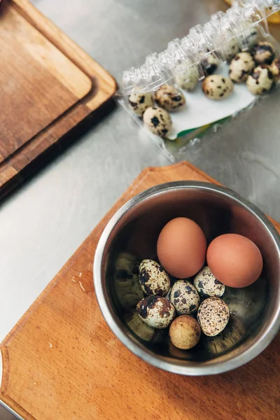 Vista superior de huevos de pollo y codorniz en cuenco de metal en la cocina - foto de stock