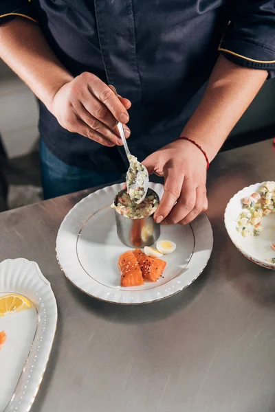 Tiro recortado de chef preparando ensalada con tubo de formación de metal y cuchara en el restaurante - foto de stock