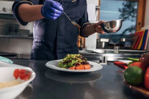 Tiro cortado de chef derramando molho na salada — Fotografia de Stock