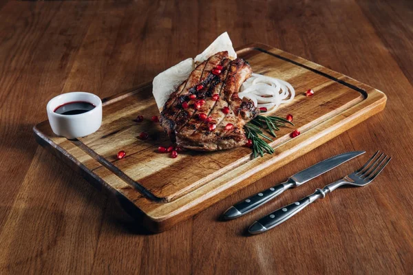 Delicioso bife grelhado servido com molho e sementes de romã em tábua de madeira — Stock Photo