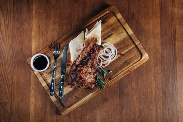 Vista superior de filete a la parrilla servido con salsa y semillas de granada en tablero de madera - foto de stock