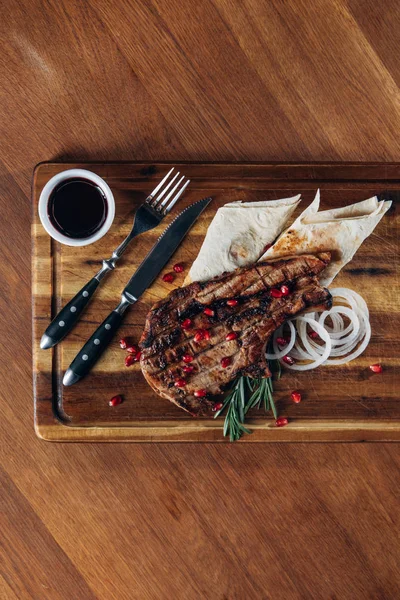 Vista superior de delicioso bife grelhado servido com molho e sementes de romã em tábua de madeira — Stock Photo