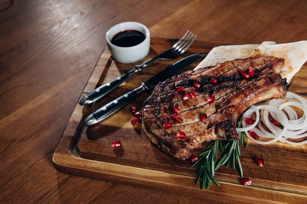Close-up shot of grilled steak served with sauce and pomegranate seeds on wooden board — Stock Photo