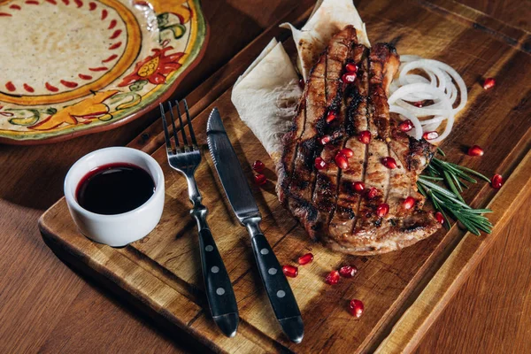 Nahaufnahme von gegrilltem Steak mit Sauce und Granatapfelkernen auf Holzbrett — Stockfoto