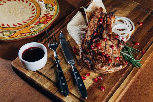 Primer plano de filete a la parrilla servido con salsa y semillas de granada en tablero de madera - foto de stock