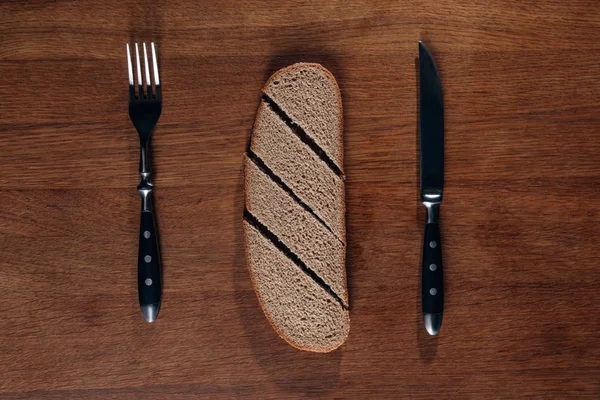 Vista superior del pan rebanado con cubiertos sobre tabla de madera - foto de stock