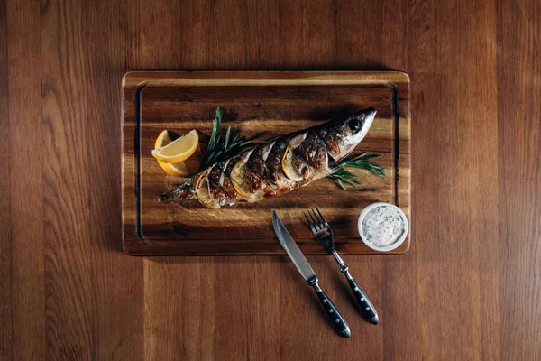 Вид вкусной рыбы на гриле с лимоном на деревянной доске — стоковое фото