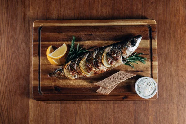 Blick von oben auf gegrillten Fisch mit Zitronen- und Roggenbrot auf Holzbrett — Stockfoto