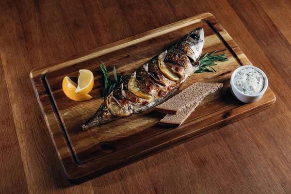 Delicious grilled fish with lemon on wooden board — Stock Photo