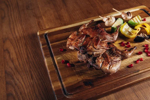 Close-up shot of roasted quail with vegetables served on wooden board — Stock Photo