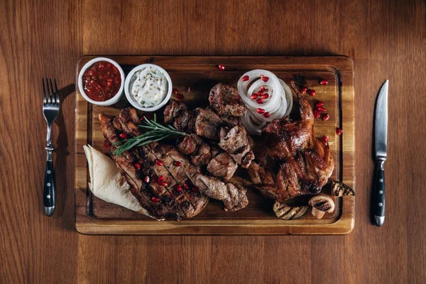 Assorted grilled meat served on wooden board with sauces — Stock Photo