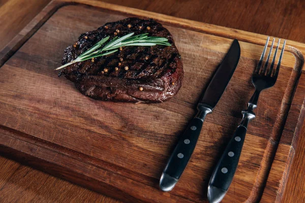 Delicioso filete a la parrilla con cubiertos en tablero de madera - foto de stock