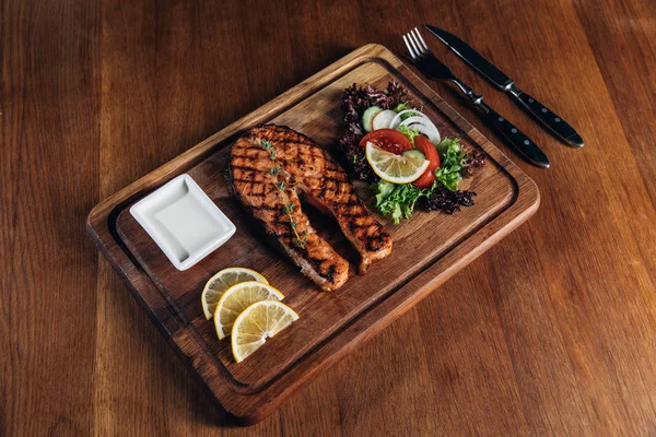 Grilled salmon steak served on wooden board with lemon and lettuce — Stock Photo