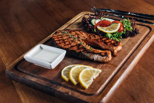 Plan rapproché de délicieux steak de saumon grillé servi sur une planche de bois avec citron et laitue — Photo de stock