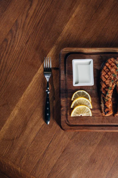 Vue du dessus du steak de saumon grillé servi sur une planche de bois avec des tranches de citron — Photo de stock