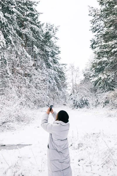 Vue arrière de la femme prenant des photos de forêt enneigée par smartphone — Photo de stock