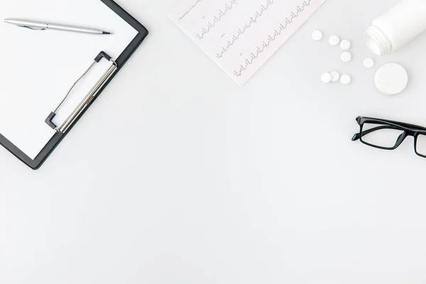 Folder with paper and pen near cardiogram and scattered pills isolated  on white background — Stock Photo