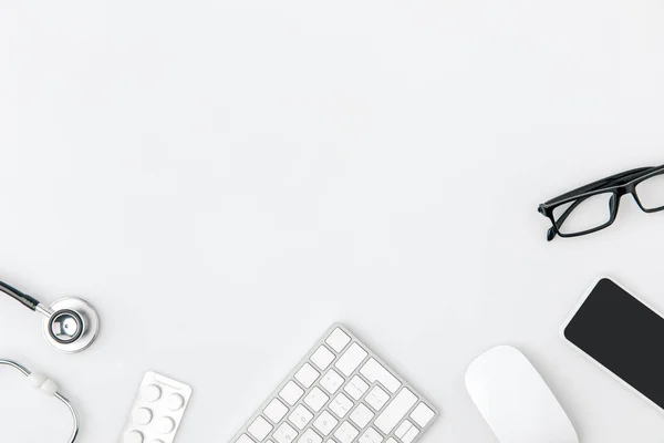 Клавіатура в оточенні окулярів, комп'ютерної миші, стетоскоп ізольовано на білому тлі — стокове фото