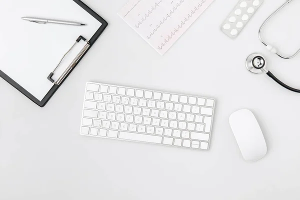 Keyboard surrounded by paper in folder, computer mouse, stethoscope isolated on white background — Stock Photo