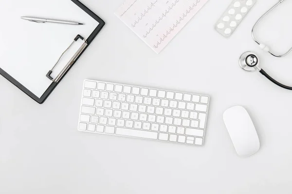 Teclado cercado por papel em pasta, mouse de computador, estetoscópio isolado em fundo branco — Fotografia de Stock