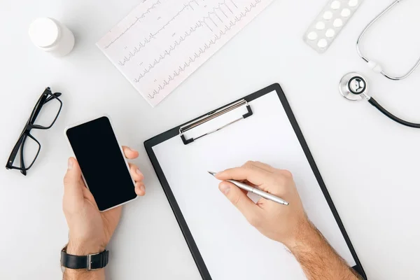 Vista superior de la mano con bolígrafo sobre papel en carpeta y smartphone en otro aislado sobre fondo blanco - foto de stock