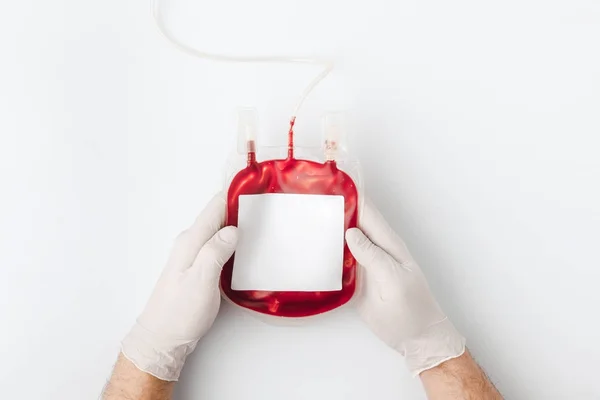 Vista dall'alto delle mani in guanti che tengono il sangue per trasfusione isolata su sfondo bianco — Foto stock