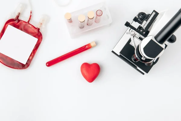 Corazón rojo contra viales con sangre y microscopio aislados sobre fondo blanco - foto de stock