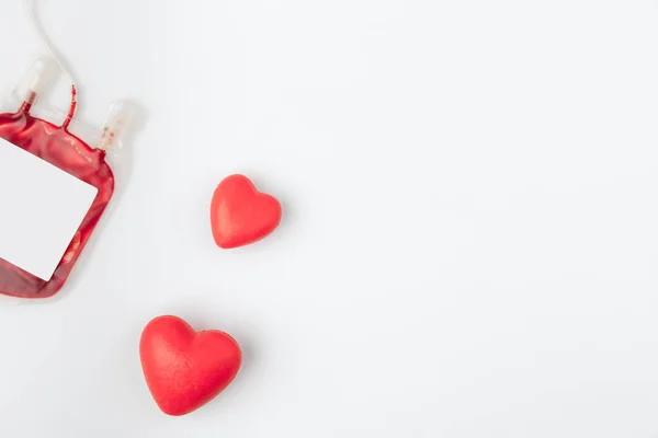 Due cuori rossi vicino al pacchetto di plastica con sangue per trasfusione isolato su sfondo bianco — Foto stock