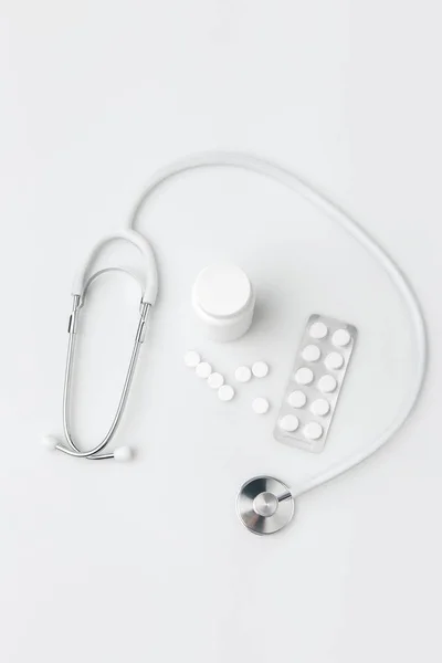 Стетоскоп, разбросанные таблетки и другие таблетки в упаковке и в пластиковой банке изолированы на белом фоне — стоковое фото