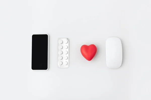 Smartphone con pantalla en blanco, pastillas, hierba y ratón de ordenador aislado sobre fondo blanco en una fila - foto de stock