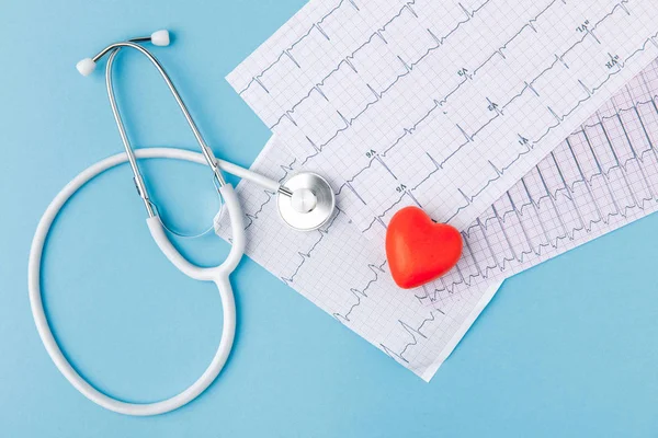 Estetoscopio, cardiograma y corazón rojo aislados sobre fondo azul - foto de stock