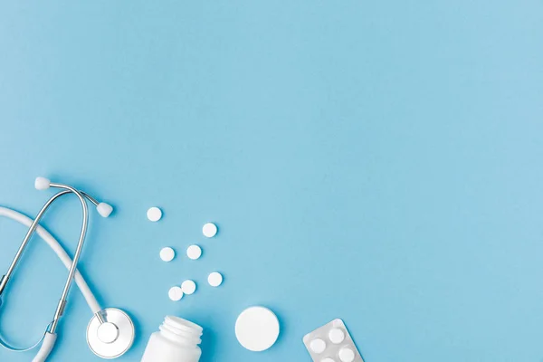 Контейнер, разбросанные таблетки и стетоскоп изолированы на синем фоне — стоковое фото