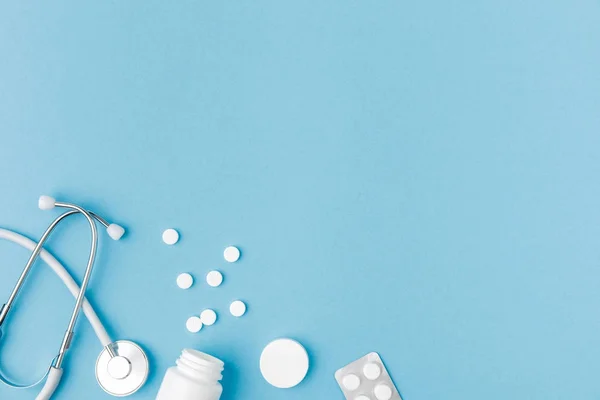 Container, scattered pills and stethoscope isolated on blue background — Stock Photo