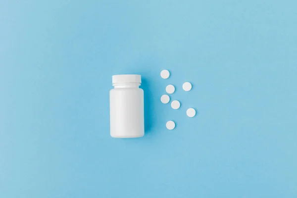 Behälter und verstreute Pillen isoliert auf blauem Hintergrund — Stockfoto