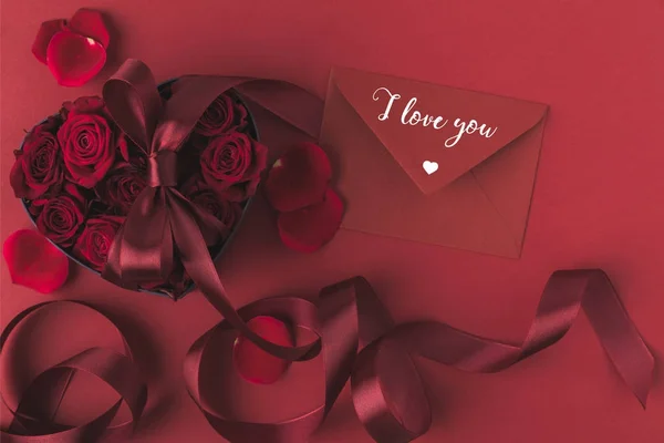Von oben Ansicht der Rosen in herzförmiger Geschenkschachtel mit Band und Umschlag isoliert auf rotem, st Valentinstag Urlaubskonzept — Stockfoto