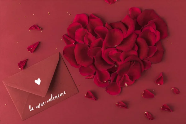 Vista dall'alto del cuore fatto di petali di rose e busta isolata su rosso, concetto giorno st valentines — Foto stock