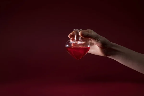 Cropped image of woman holding heart shaped glass jar of perfume isolated on red — Stock Photo